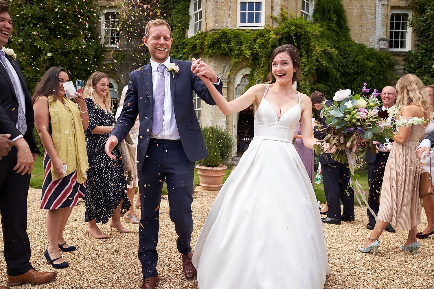Wedding guests shower joyful couple with confetti outside a grand country estate on their special day.