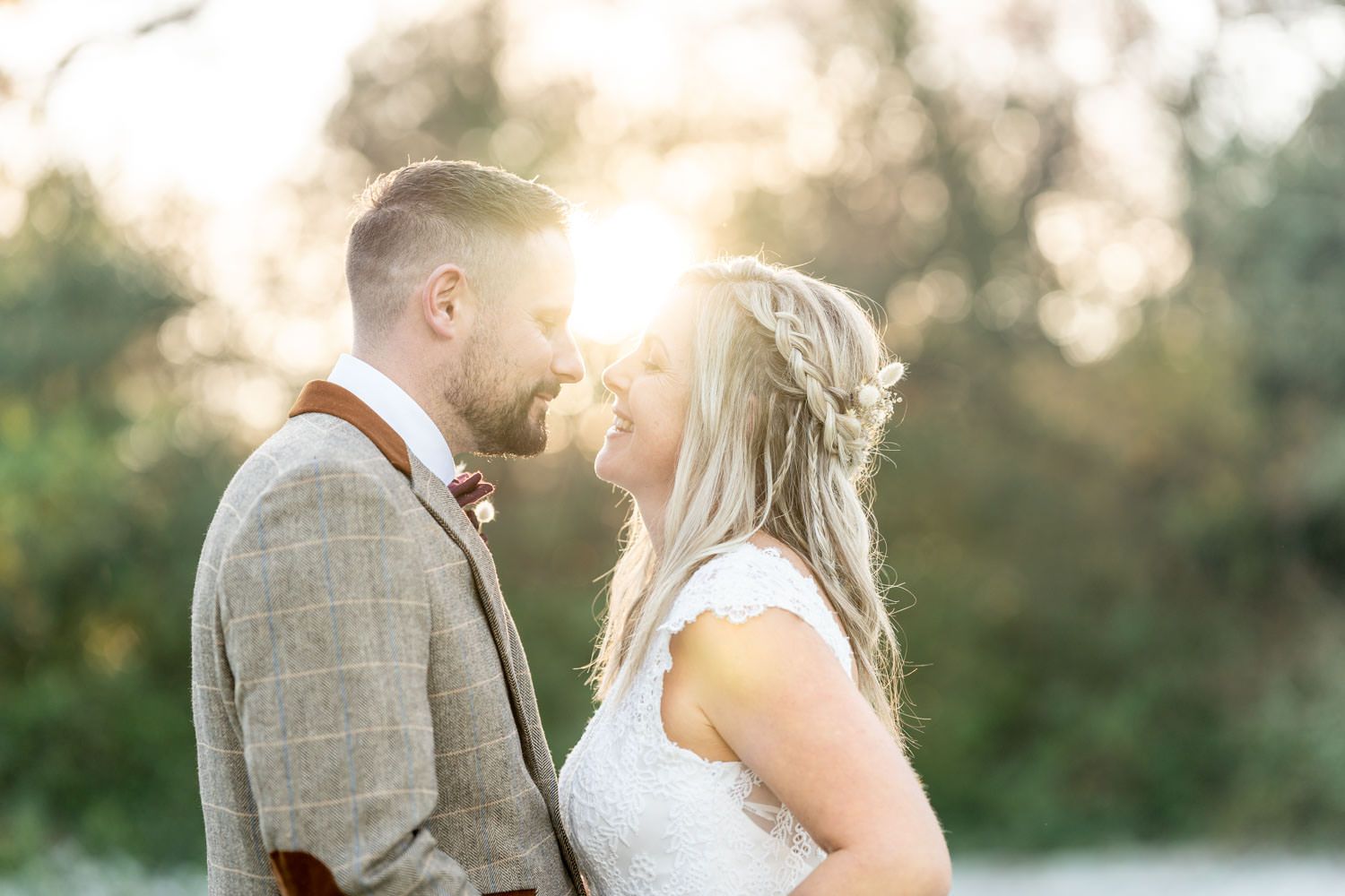 A romantic couple in wedding attire sharing an intimate moment at sunset in a natural outdoor setting.
