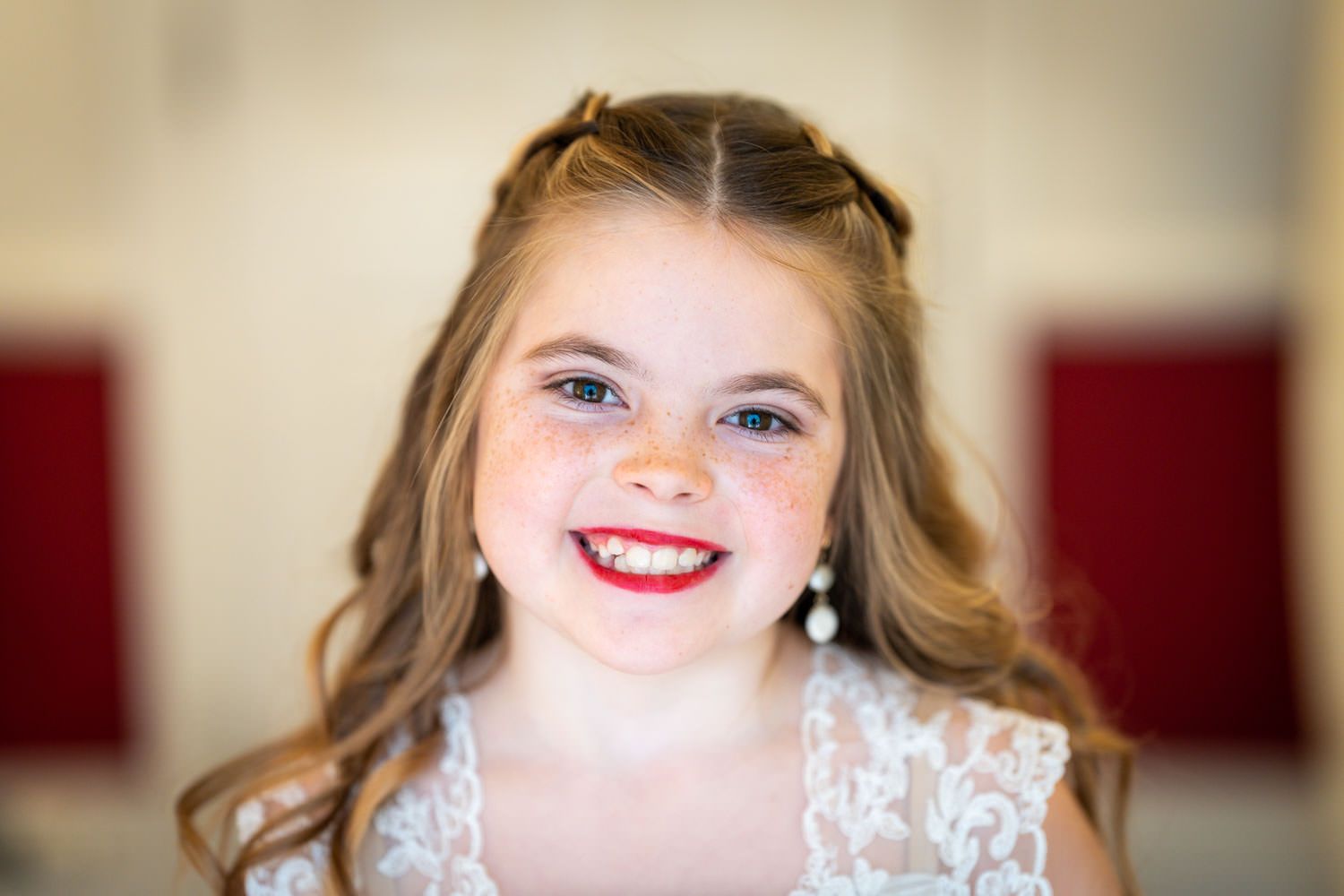 A bright smile radiates joy while wearing a delicate white lace dress and dangling earrings.
