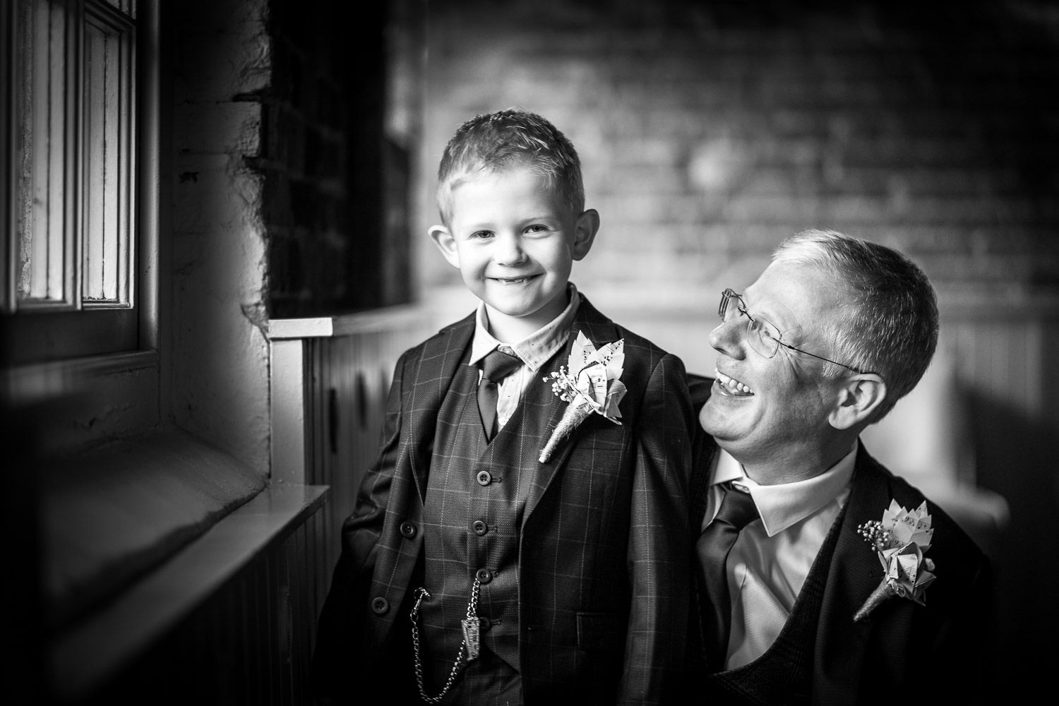 A heartwarming black and white candid moment shared between a man and young boy wearing matching buttonhole flowers.