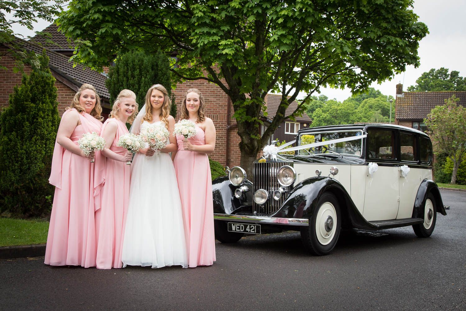 A classic vintage Rolls Royce wedding car parked next to people in pink and white formal dresses.