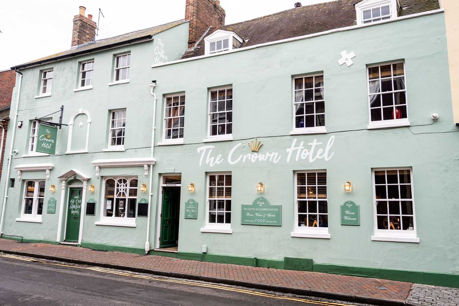 A pale mint green Georgian hotel building with white-framed windows and vintage shop fronts along a quiet street.