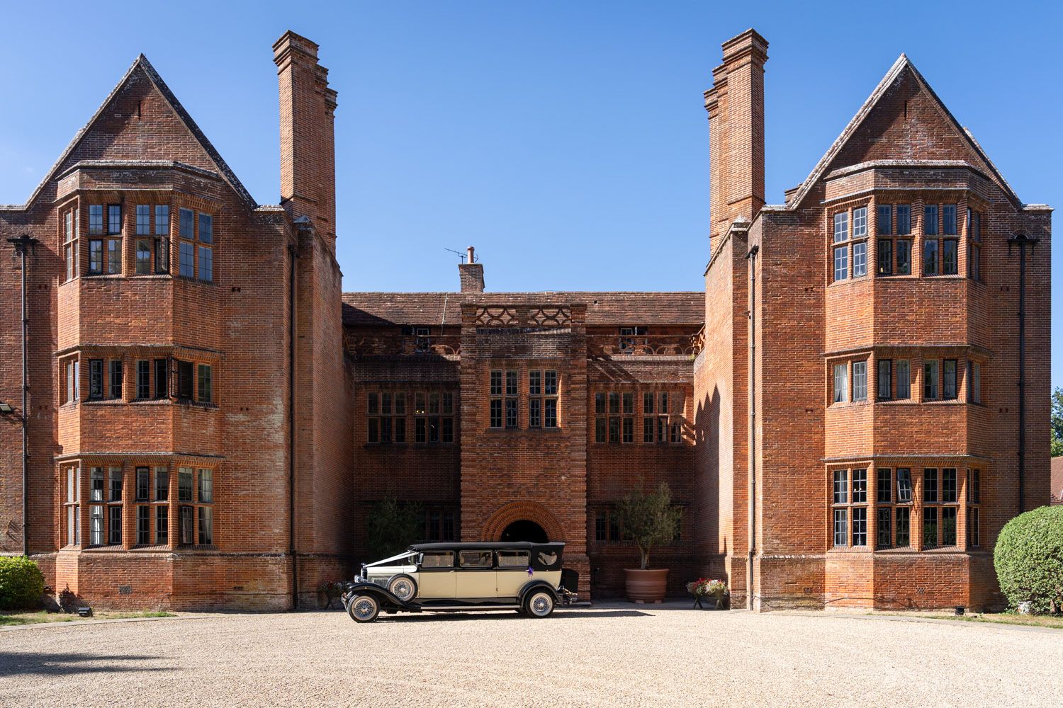 Classic vintage wedding car parked outside grand red brick English manor house wedding venue.