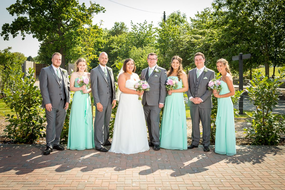 Wedding party in gray suits and mint green dresses posed together on a garden patio.