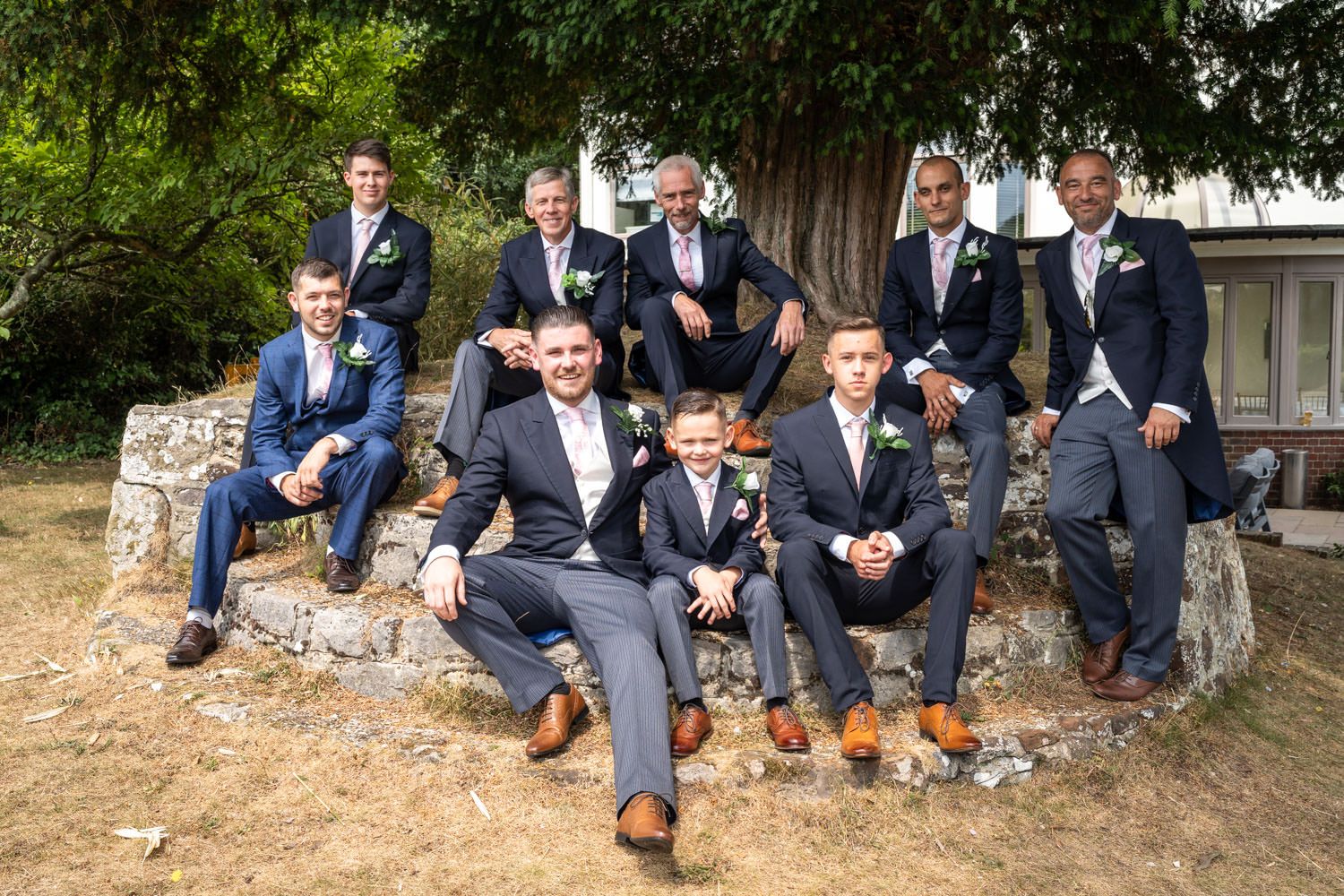 A group wearing coordinated navy and gray formal attire poses together on rustic stone steps outdoors.
