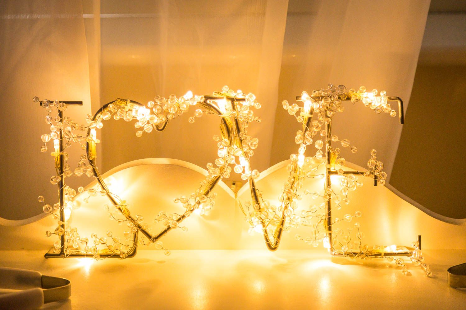 Wire shaped to spell LOVE illuminated with warm white fairy lights glows against a golden backdrop.