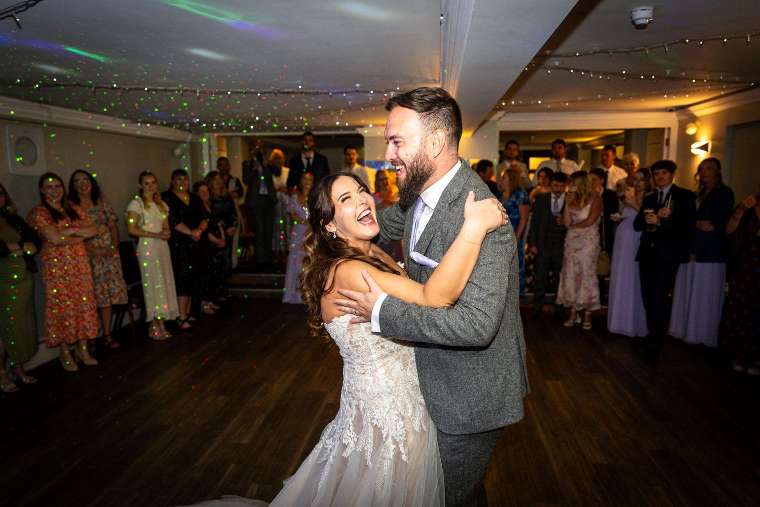 Bride and groom sharing their first dance surrounded by guests at a romantic wedding reception.