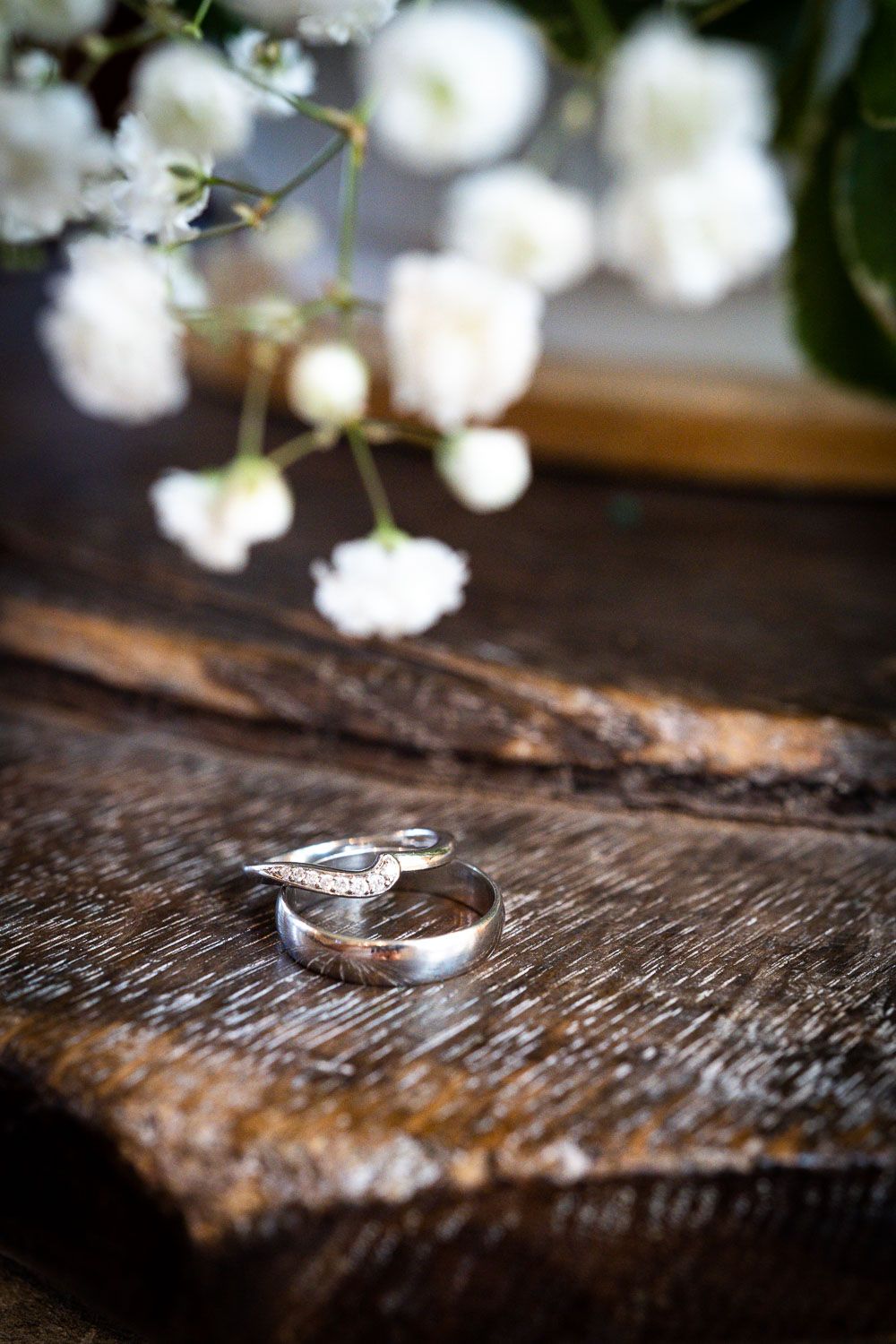 Wedding rings rest on rustic wooden surface with delicate white baby's breath flowers in soft focus background.