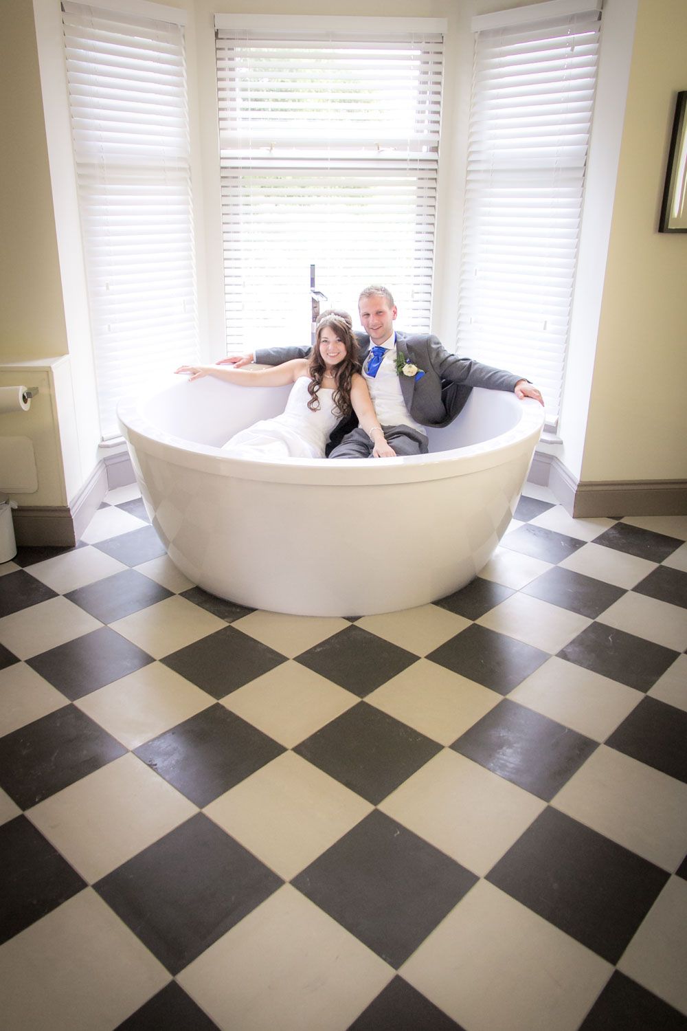 A creative of a wedding couple in a bath tub on a black and white checkered floor.