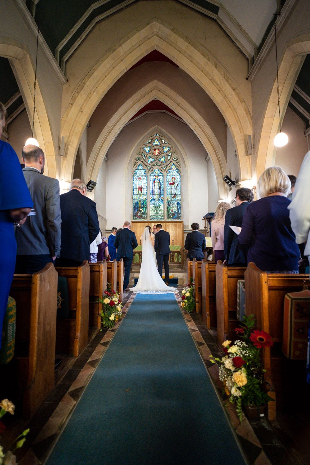 Elegant church wedding ceremony with stained glass windows and floral-lined aisle in traditional chapel interior.