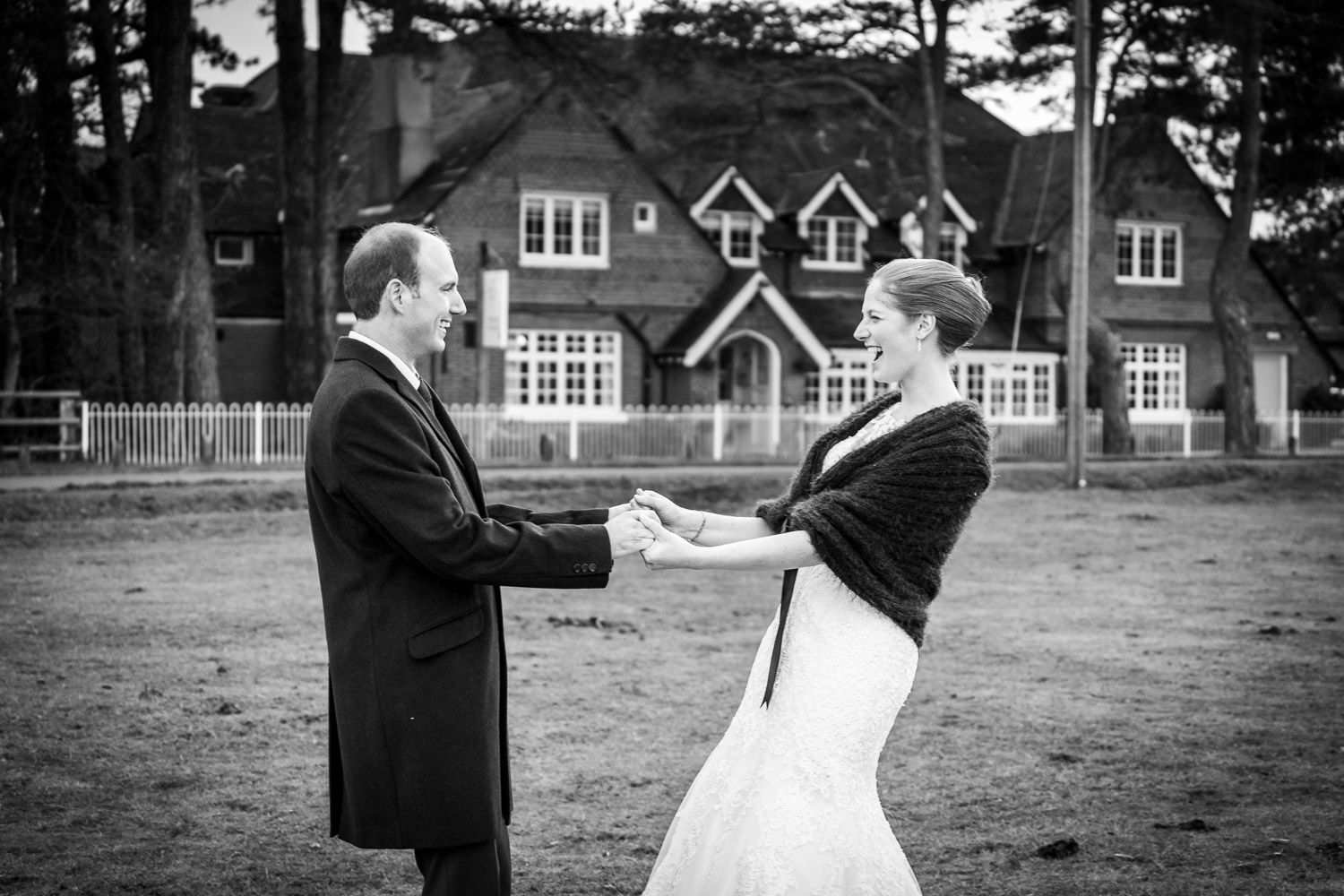 Black and white photo of a couple dancing outdoors in front of a brick Tudor style house.