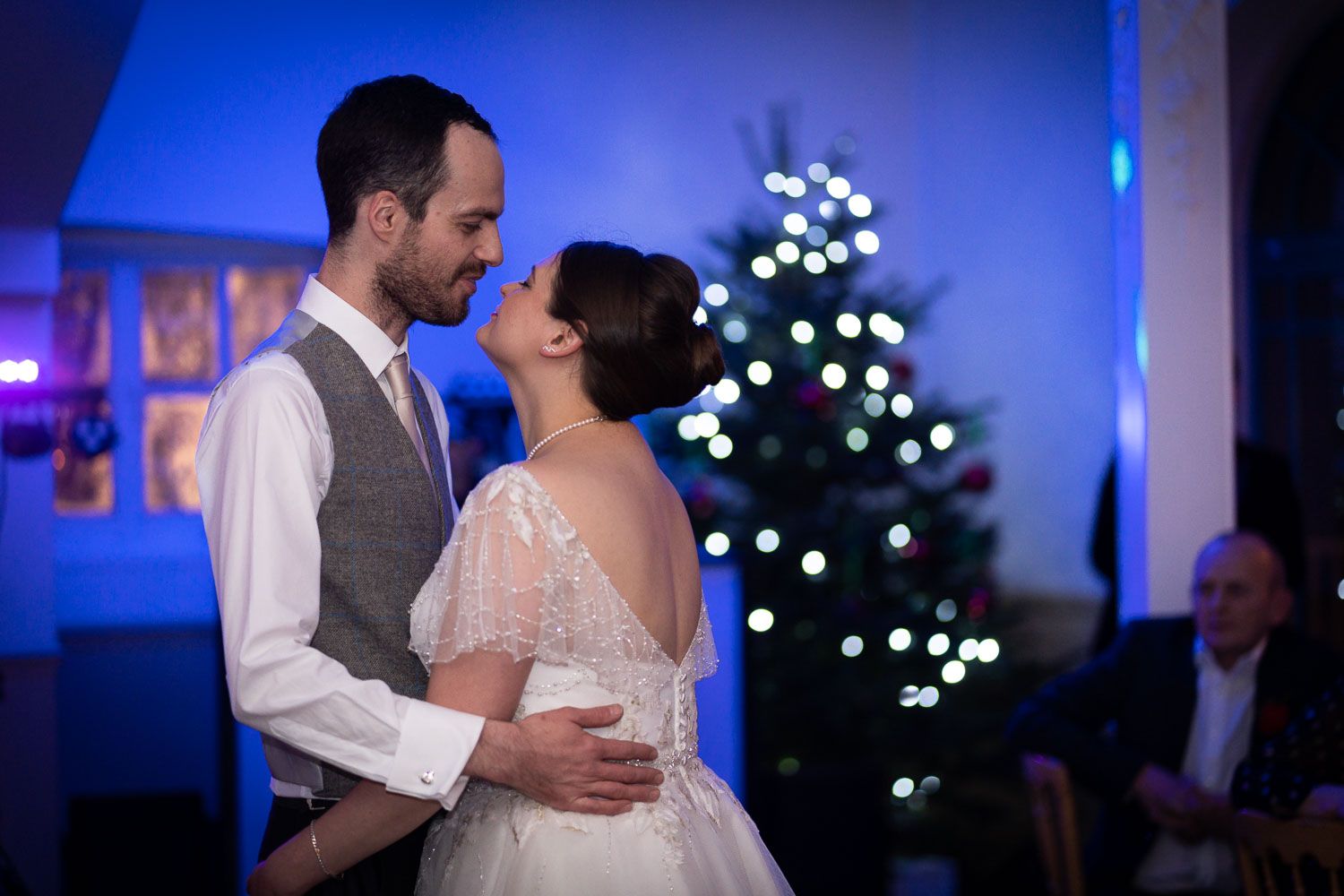 A romantic dance between a couple in wedding attire with a glowing Christmas tree in the background.