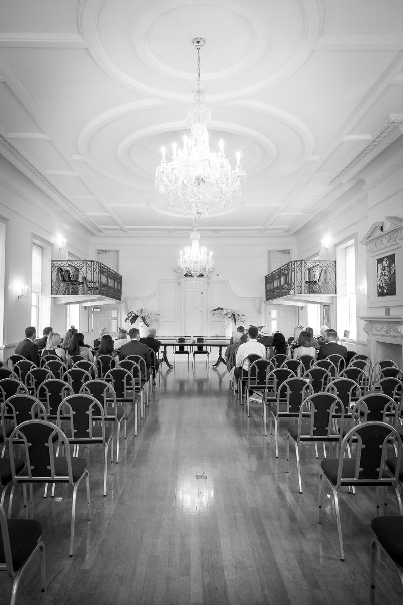 Interior of an elegant wedding venue with crystal chandeliers, rows of chairs, and ornate white walls and ceiling details.