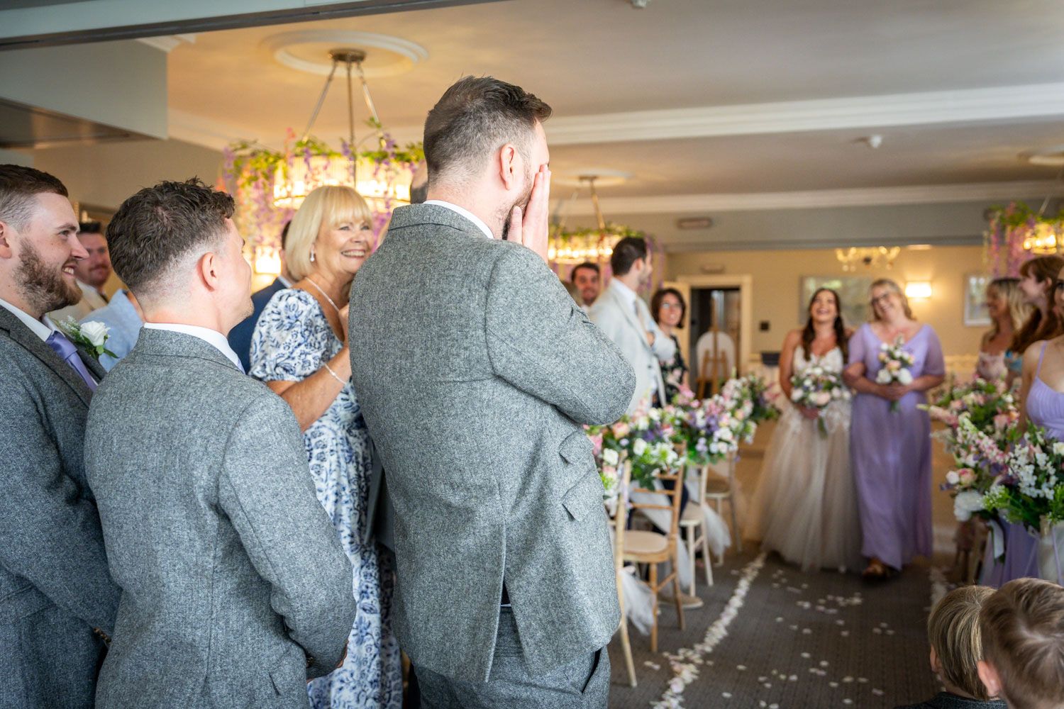 Emotional groom covering his face as bride walks down the aisle at an elegant wedding venue.
