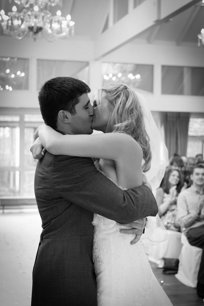 A romantic black and white photo of a couple sharing their first dance at their wedding reception with chandeliers above.