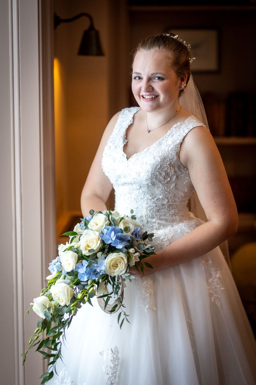 Bridal portrait with white and blue bouquet by window in natural light.