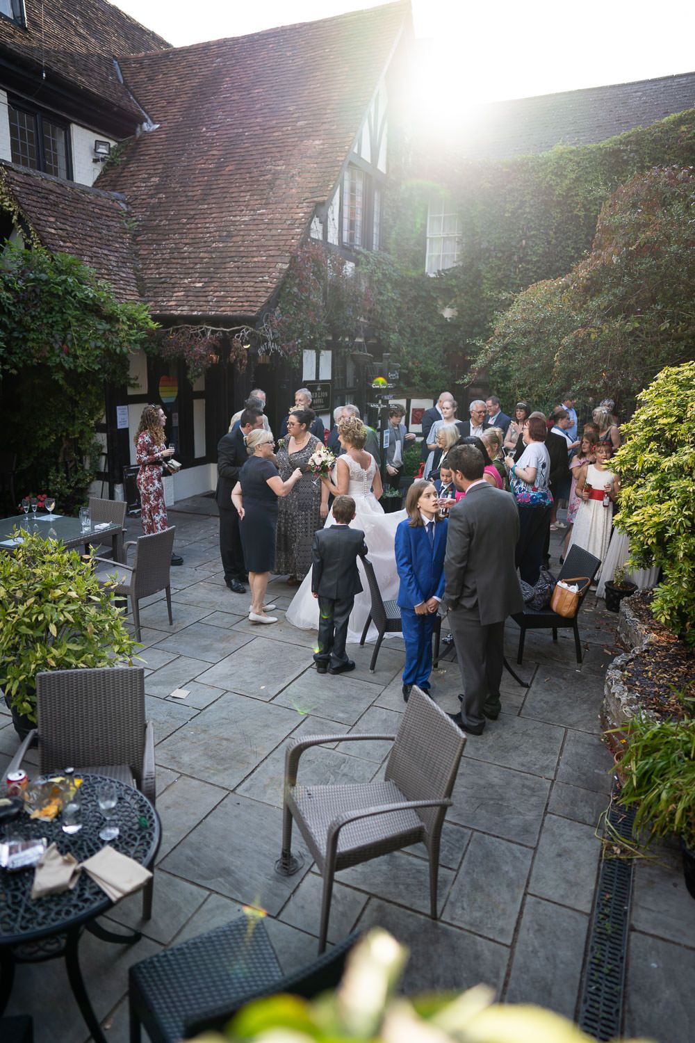 Guests mingle during an outdoor reception on a stone patio at dusk beside a Tudor-style building.