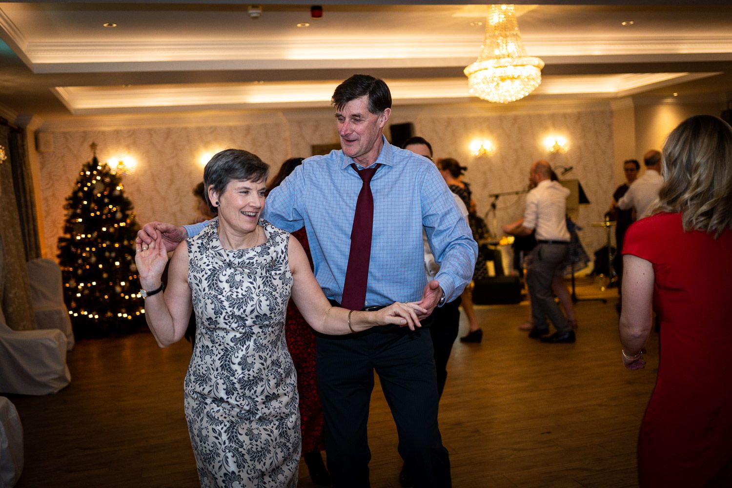 Couples dancing at a winter wedding reception with a decorated Christmas tree visible in the background.