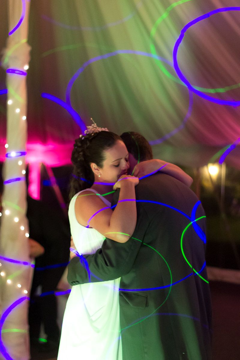 A couple shares a romantic slow dance under colorful lights and swirling projections at a wedding reception.
