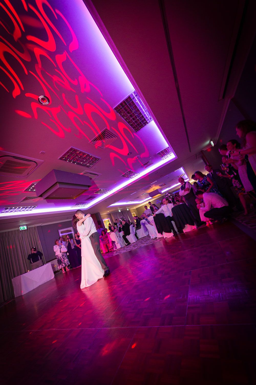 A wedding dance floor illuminated with dramatic purple and red lighting creates an atmospheric party scene.