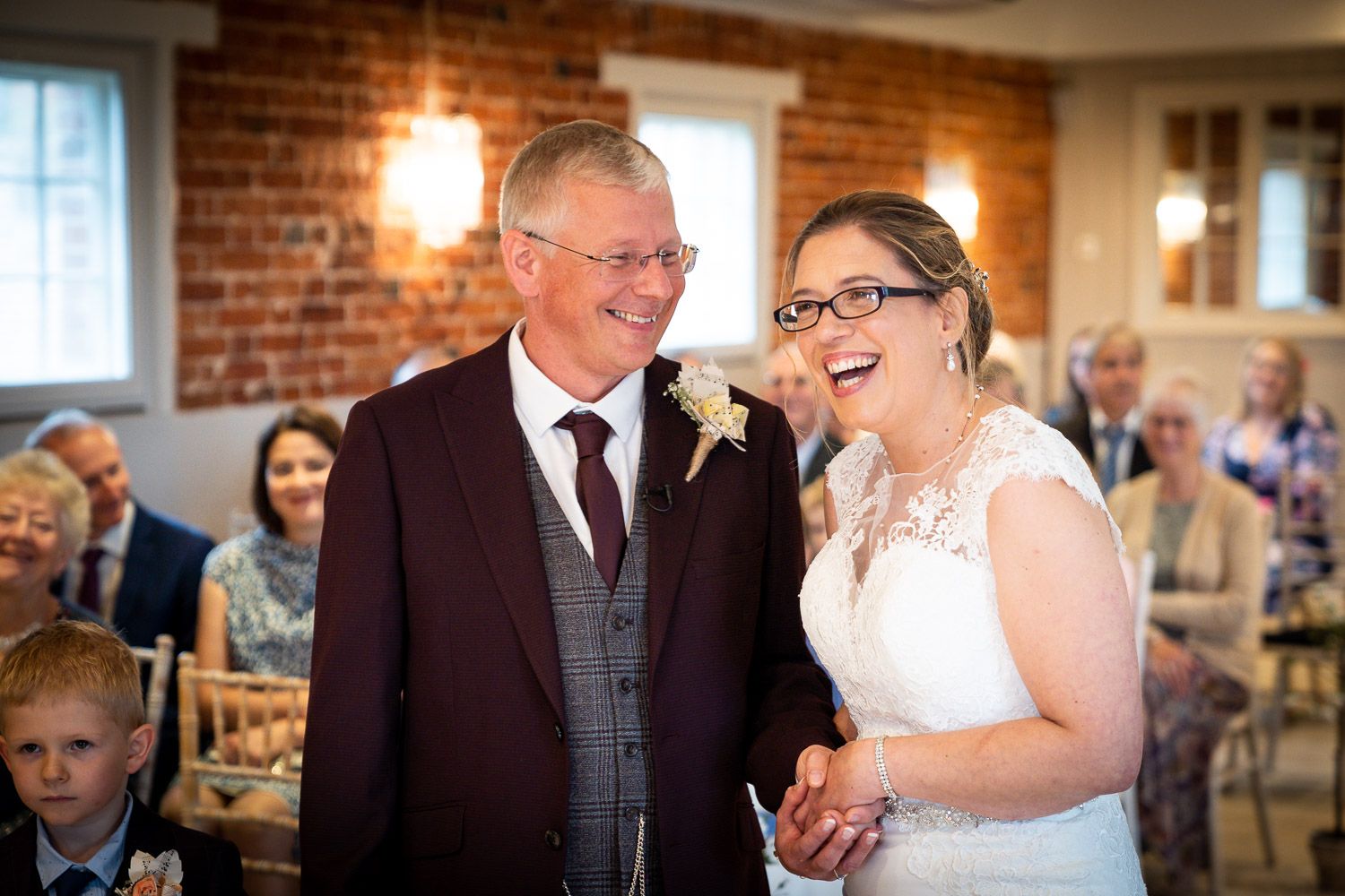 A joyful couple shares a candid laugh together during their wedding ceremony in a rustic brick-walled venue.