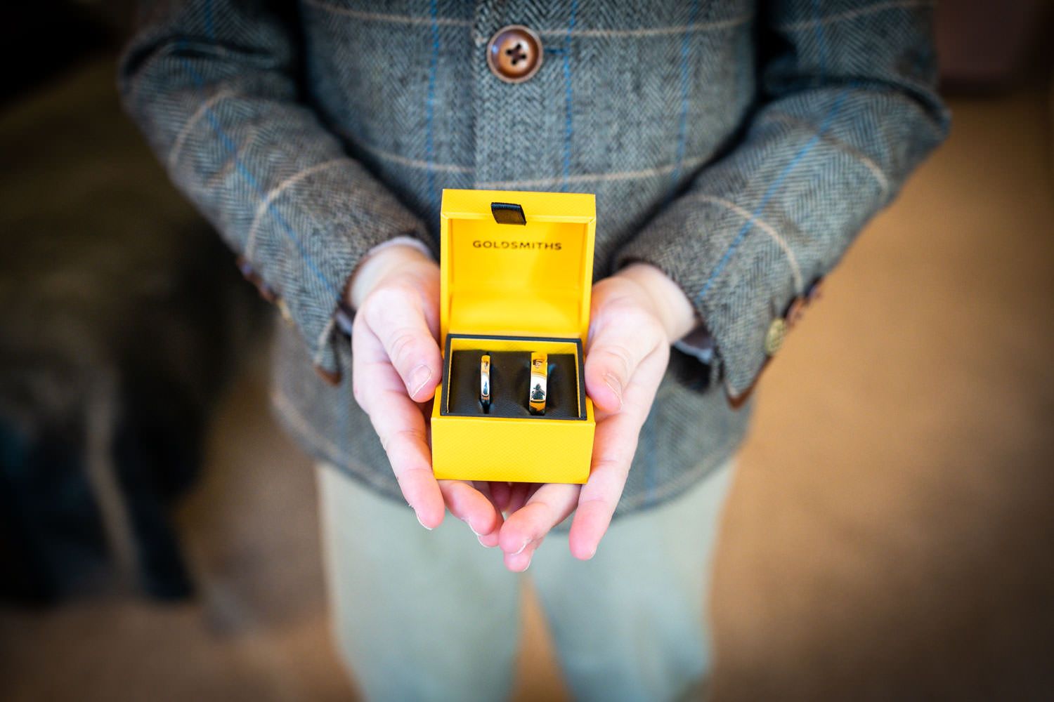 A person wearing denim holds a small black engagement ring box with a yellow interior.