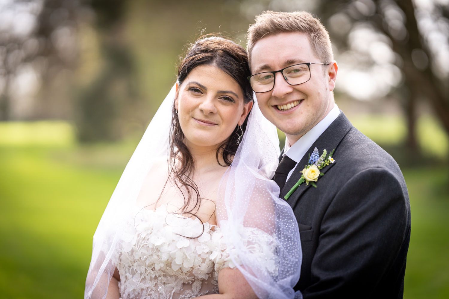 A bride and groom smile together outdoors on their wedding day with a natural green background.