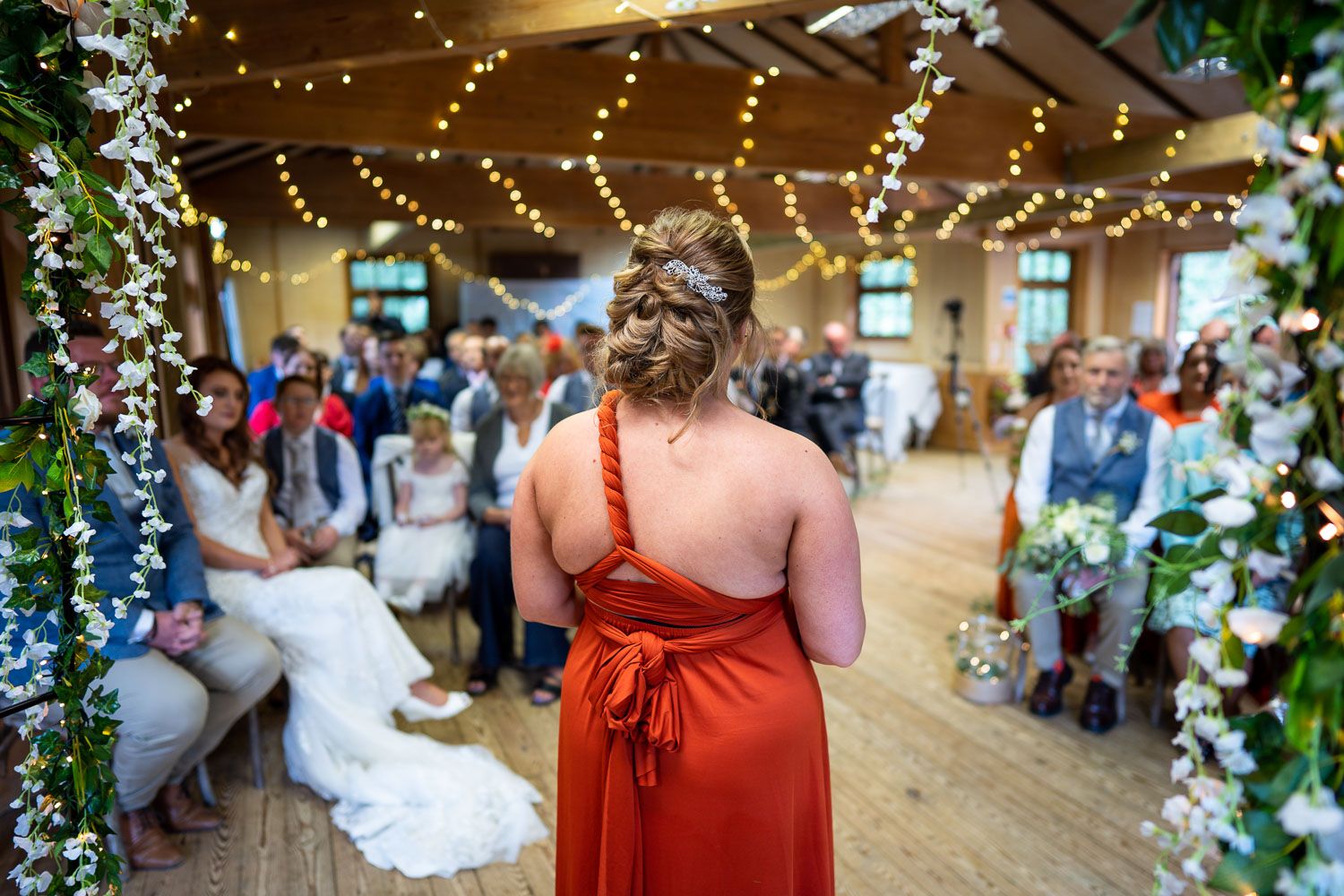 A wedding reception venue decorated with twinkling lights and greenery features people gathered for a celebration.