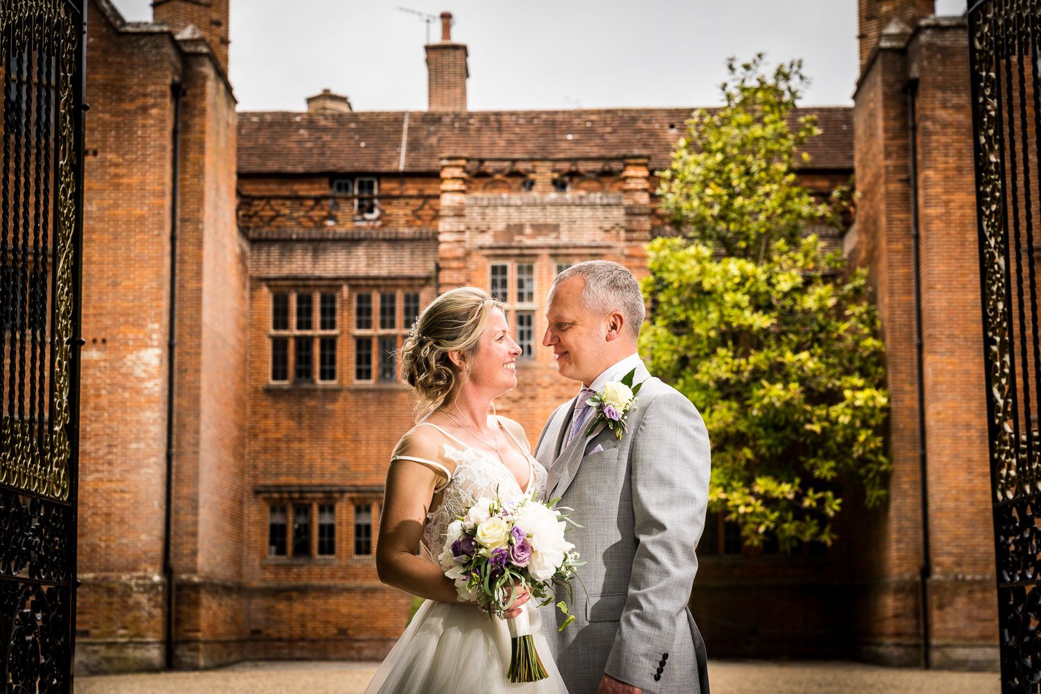 A bride and groom share a romantic moment in front of a historic building with stone walls and grand architecture.