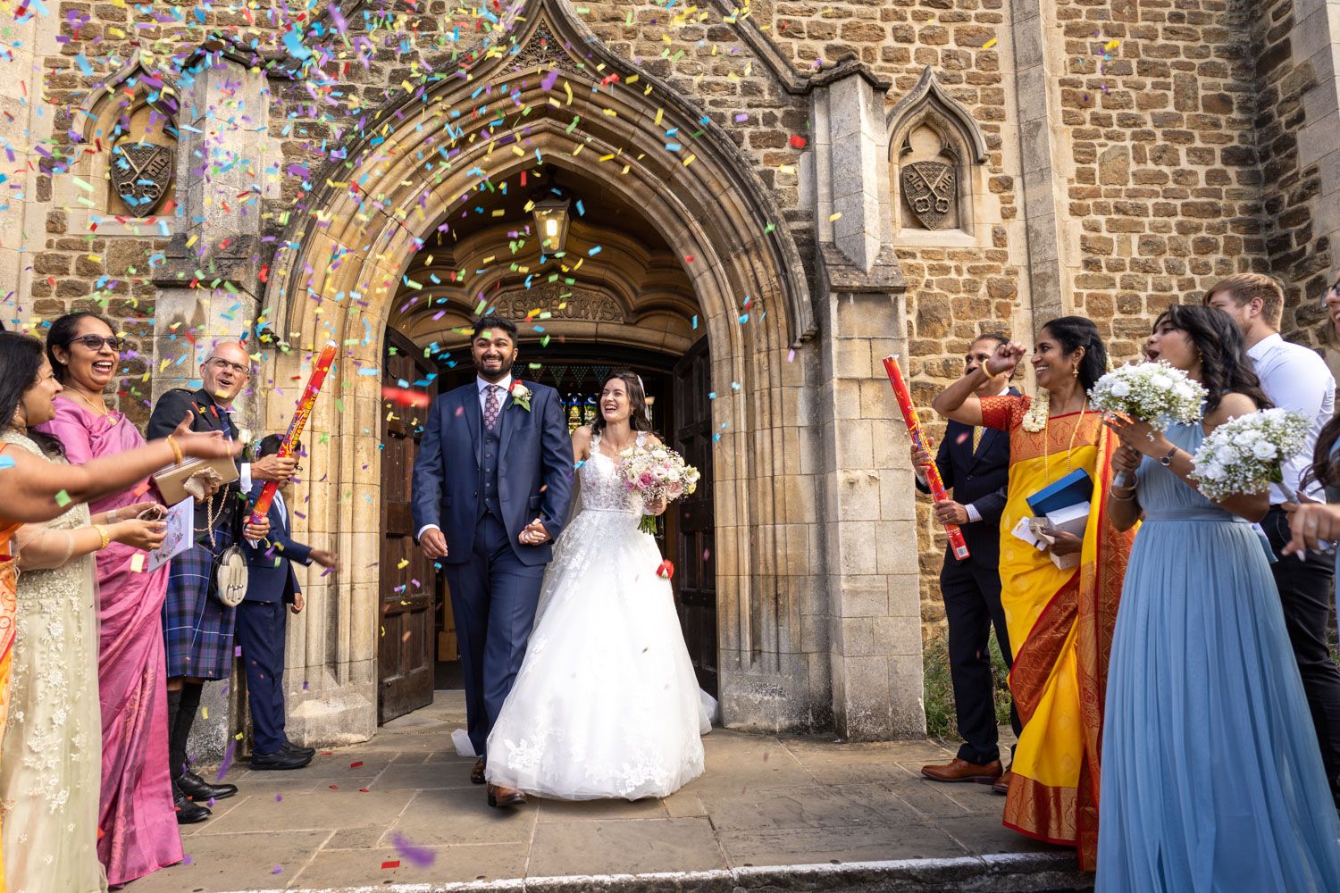 Celebrants toss colorful confetti outside a stone church's ornate Gothic archway during a wedding ceremony.
