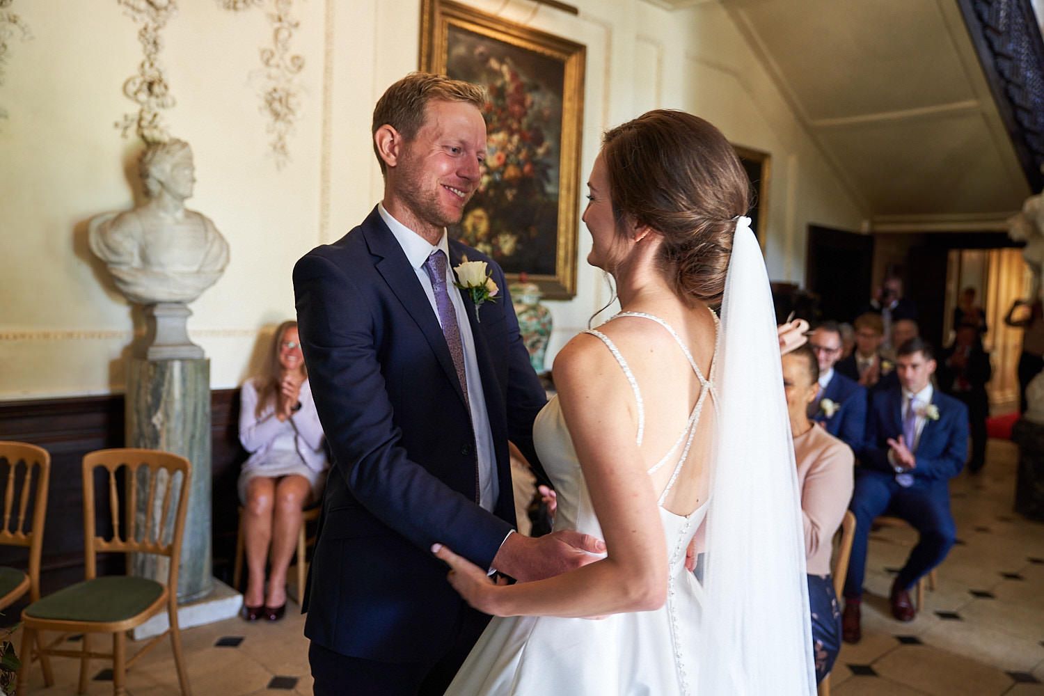 A romantic moment between newlyweds during their wedding ceremony in an elegant indoor venue with ornate decor.