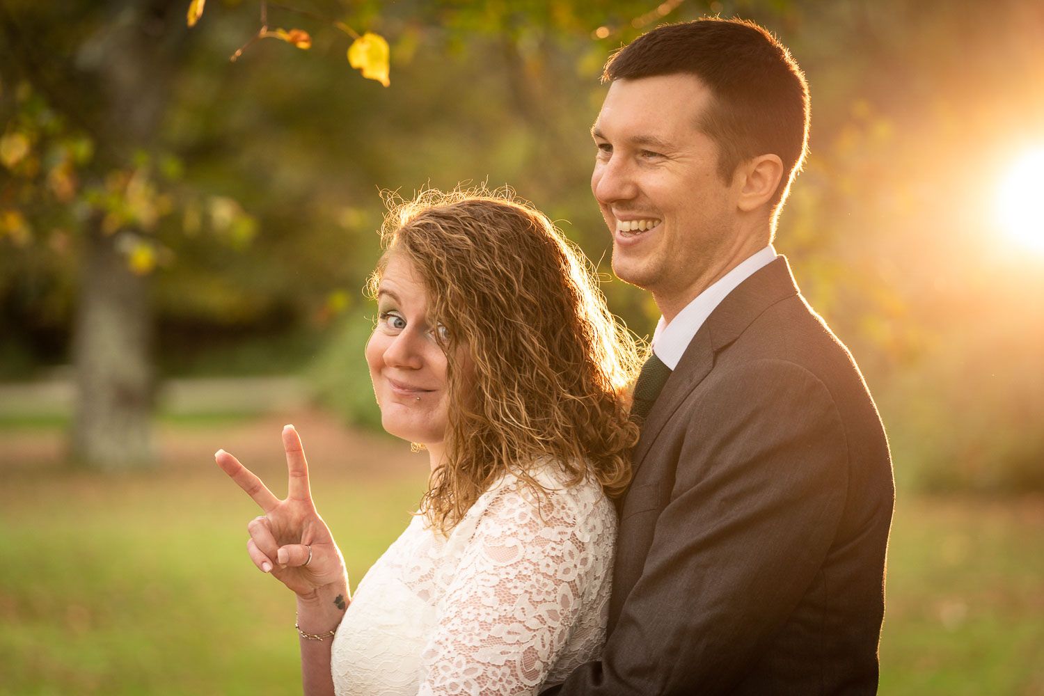 A couple poses together outdoors at sunset with glowing golden light filtering through trees in the background.