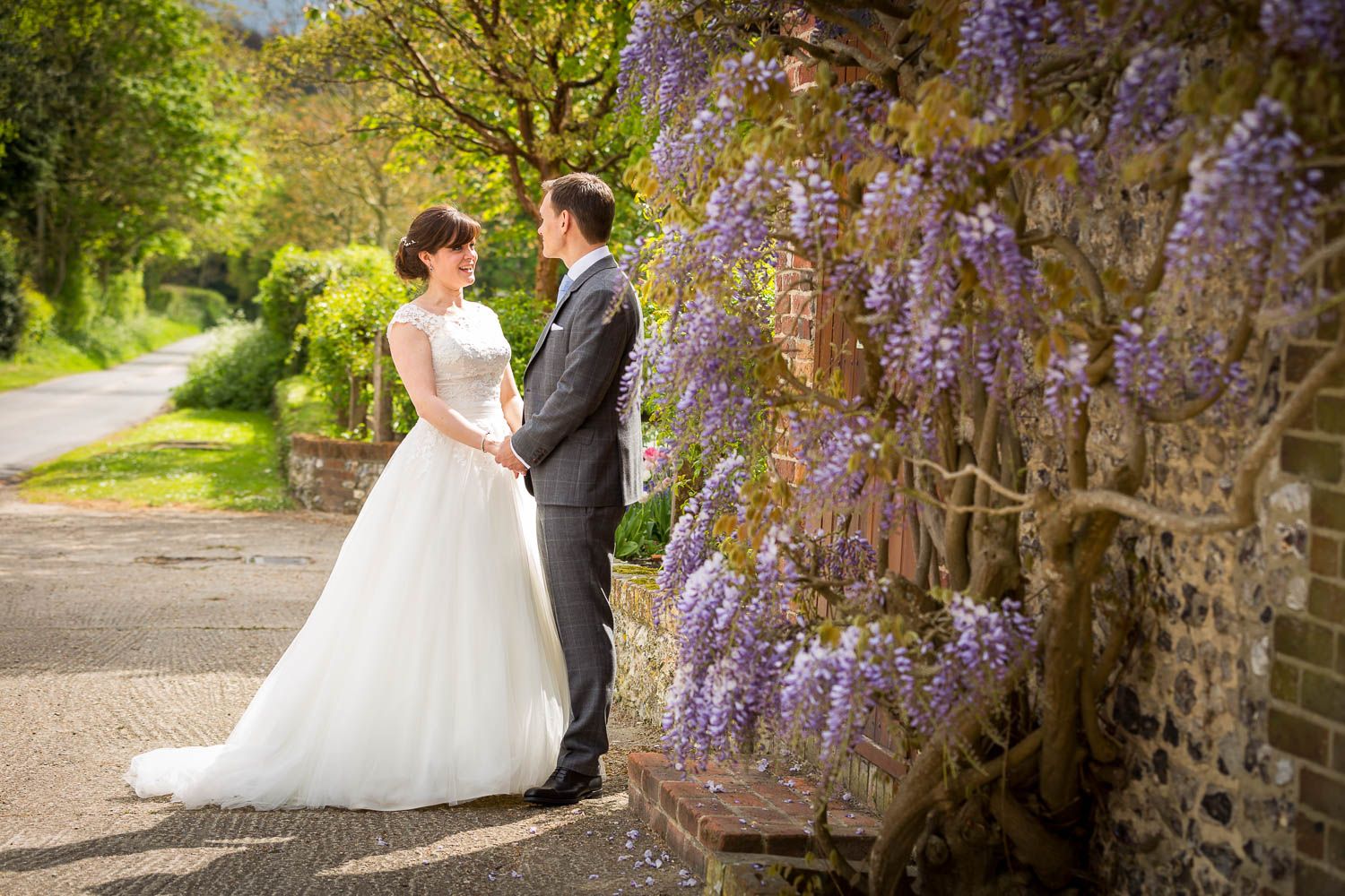A romantic wedding scene with wisteria blooms cascading down a stone wall beside a garden path.