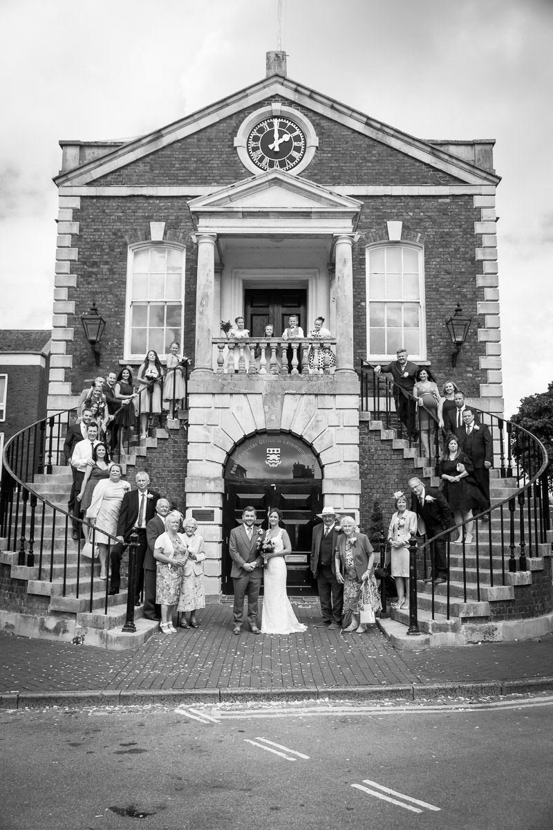 Vintage black and white photo of a wedding party gathered on the steps of a brick building with a clock tower.