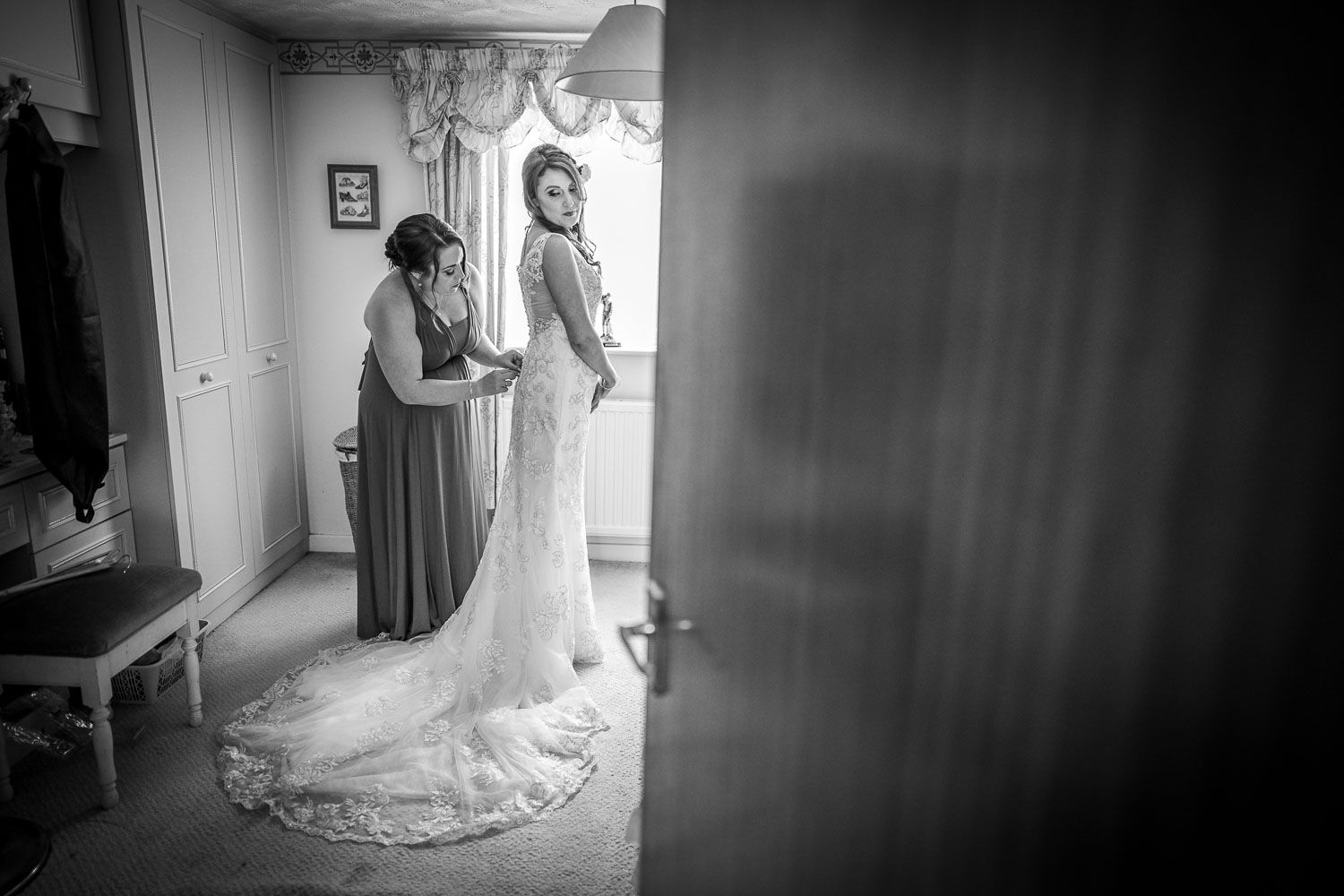 A touching black and white moment captured during wedding preparations, with a beautiful trailing lace dress in view.