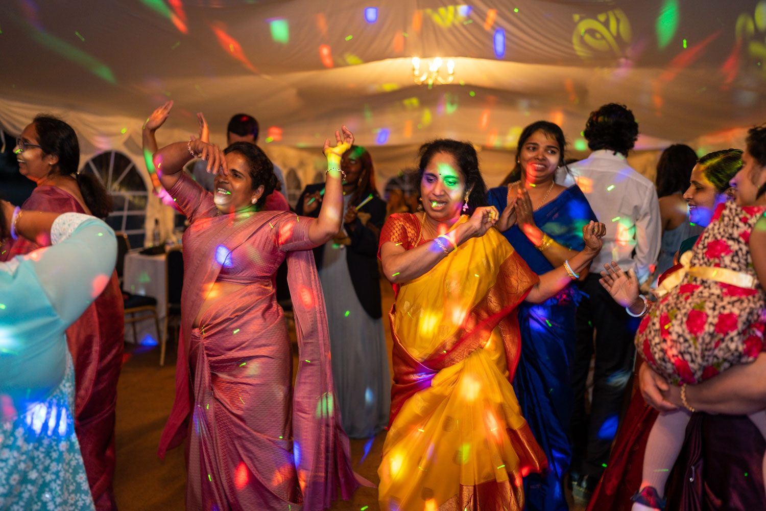 Festive party scene with colorful saris and dance lighting showing joyful celebration at an Indian wedding reception.