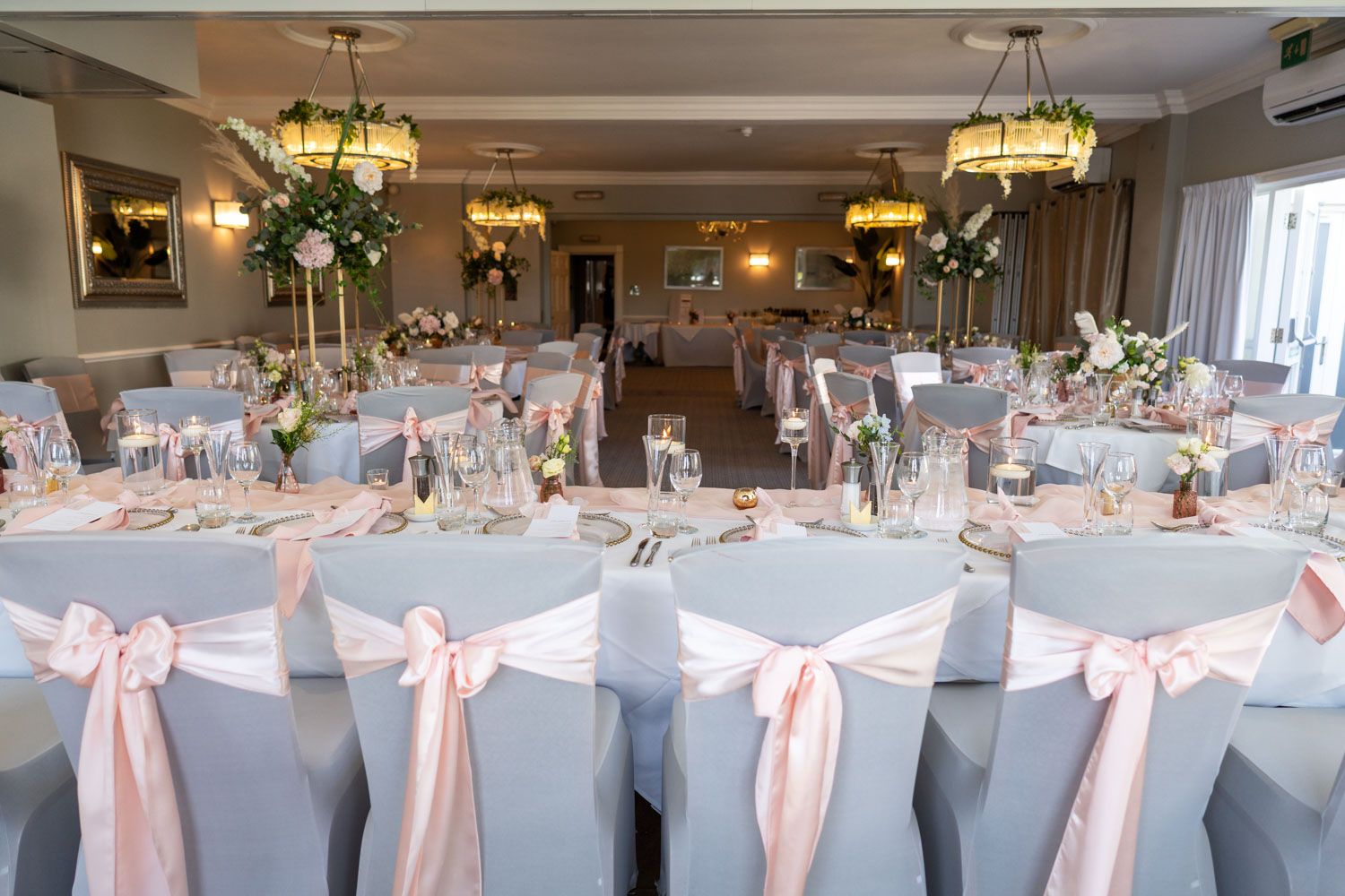 Elegant wedding reception venue with round tables decorated in white linens, pink sashes and crystal chandeliers.