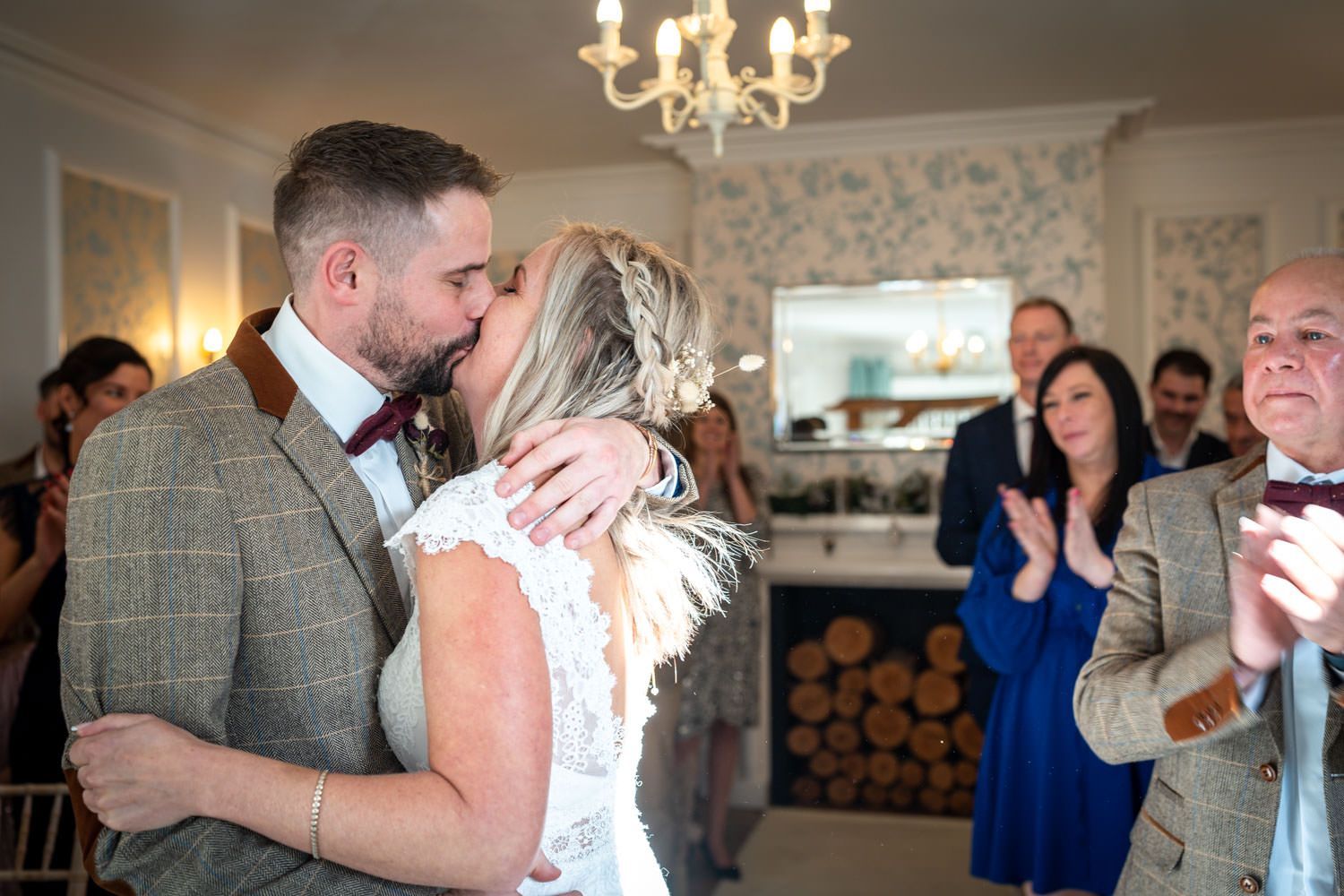 Couple embraces during wedding celebration while guests in blue dresses look on.