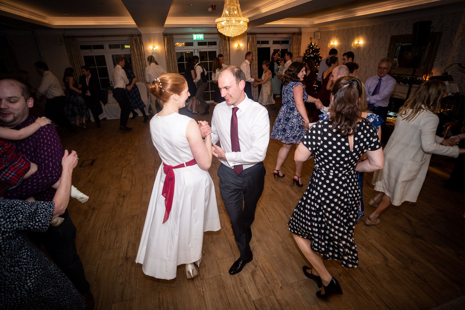 People dancing together at an elegant ballroom reception with warm lighting and hardwood floors.