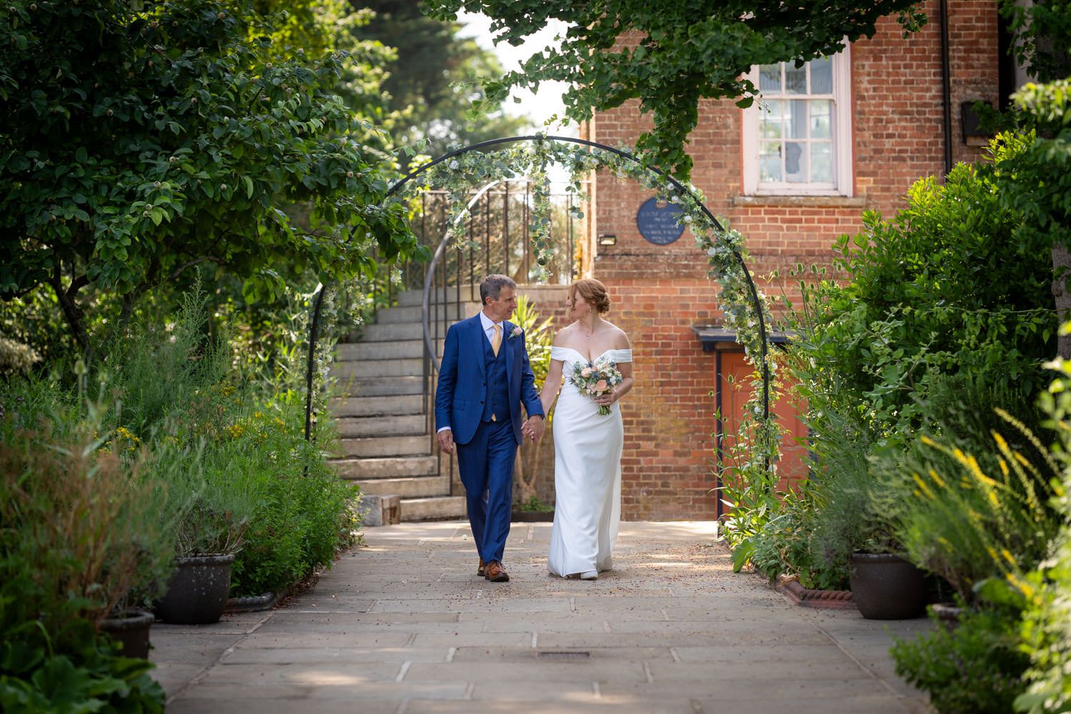 Bride and groom walking hand in hand through a beautiful garden archway on their wedding day.
