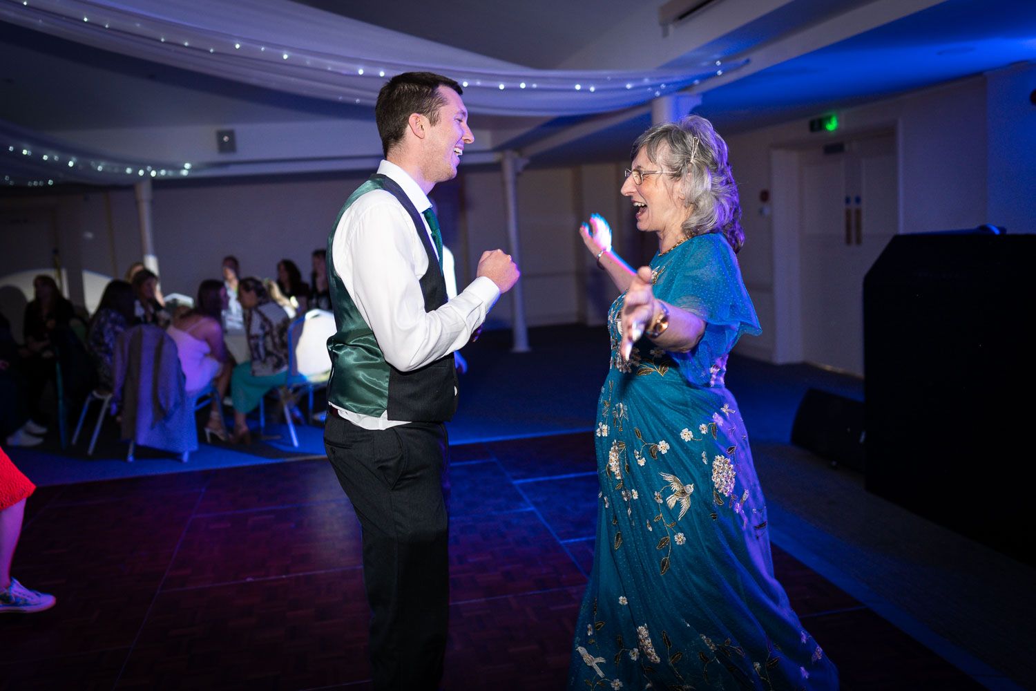 People dance together on a dark dance floor illuminated by blue lighting at a formal event.