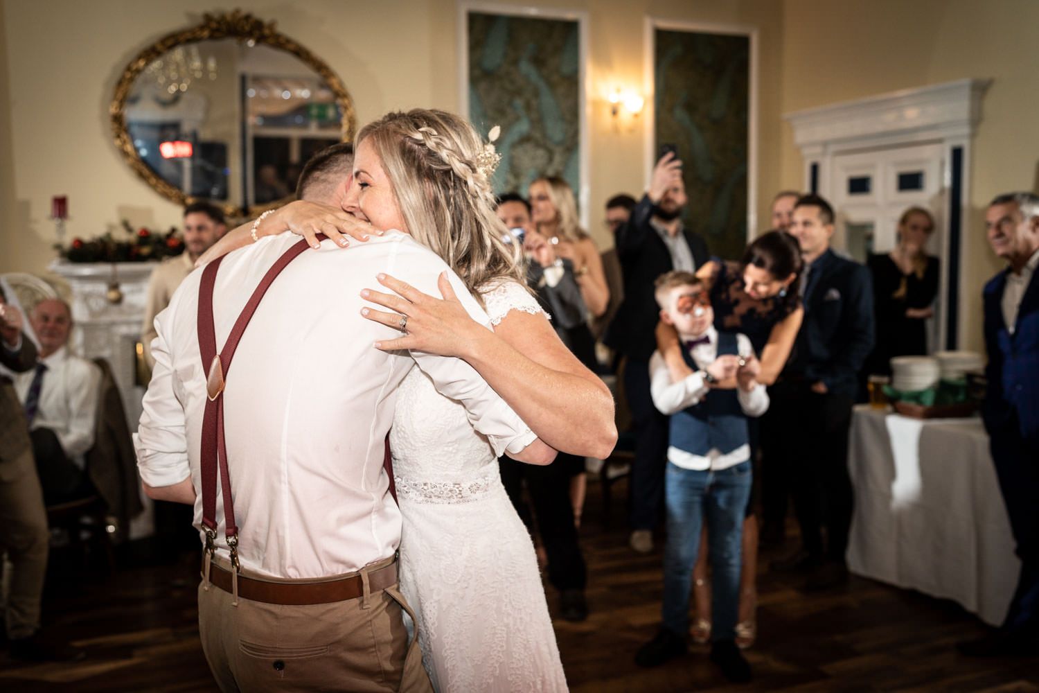 A couple shares a romantic dance at a wedding reception while guests look on and take photos in an elegant venue.