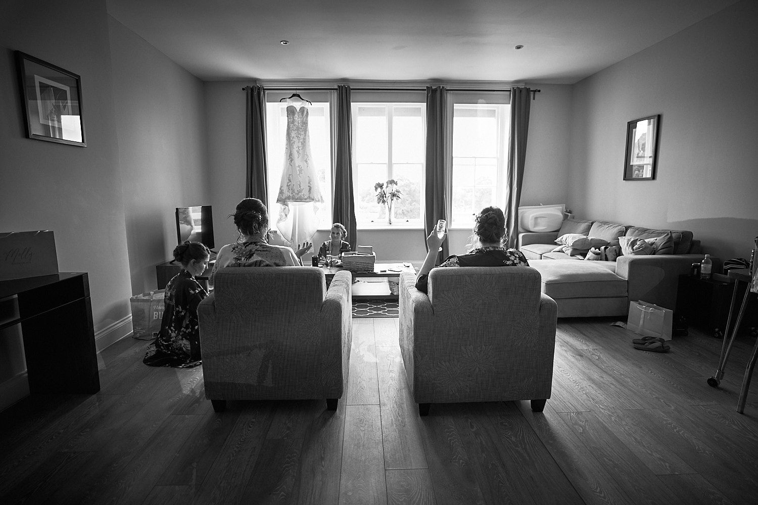 People seated in armchairs facing a window in a monochrome living room with hardwood floors.