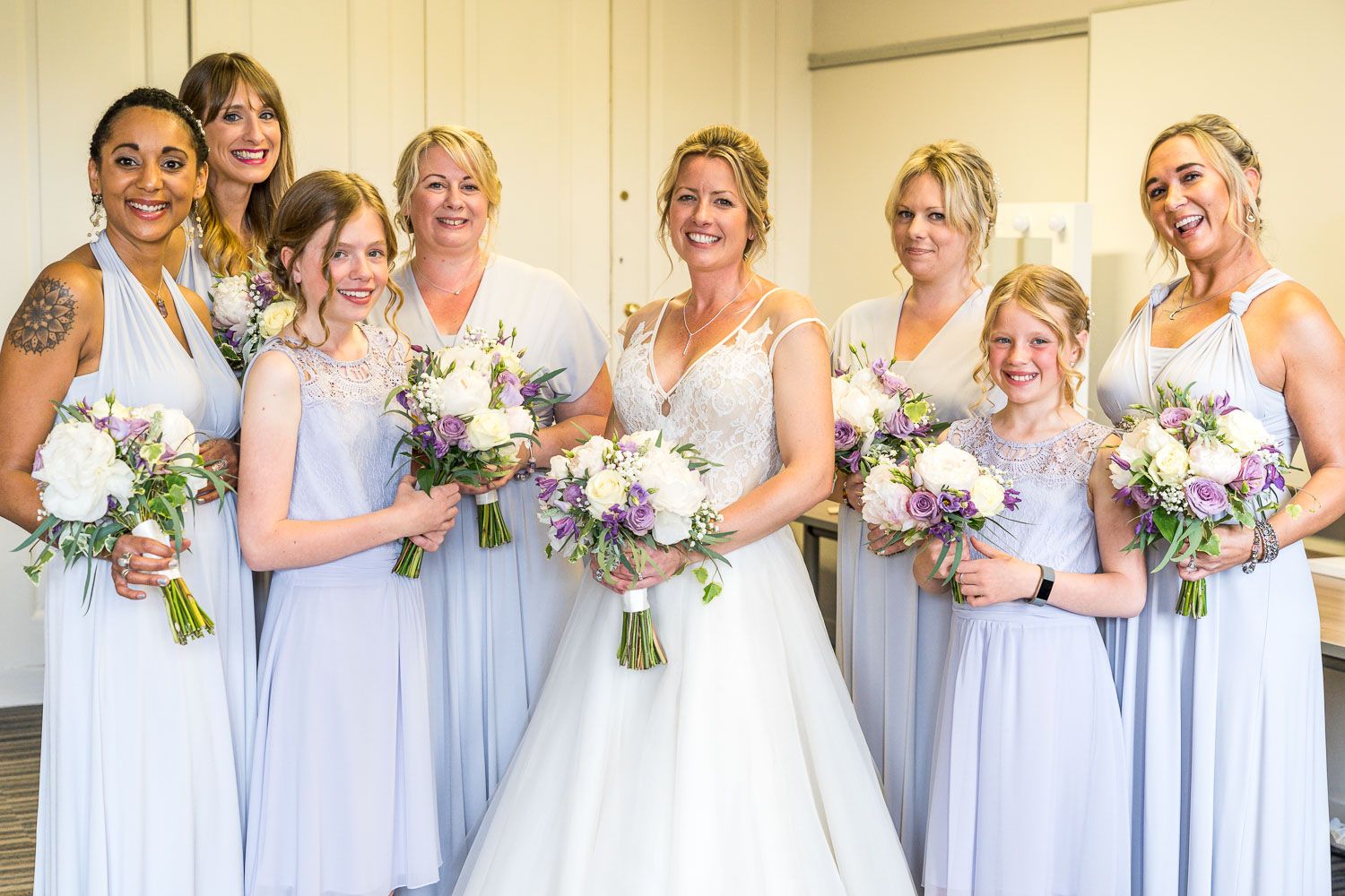 Bridesmaids in matching pale blue gowns holding pastel bouquets pose with bride in white wedding dress.