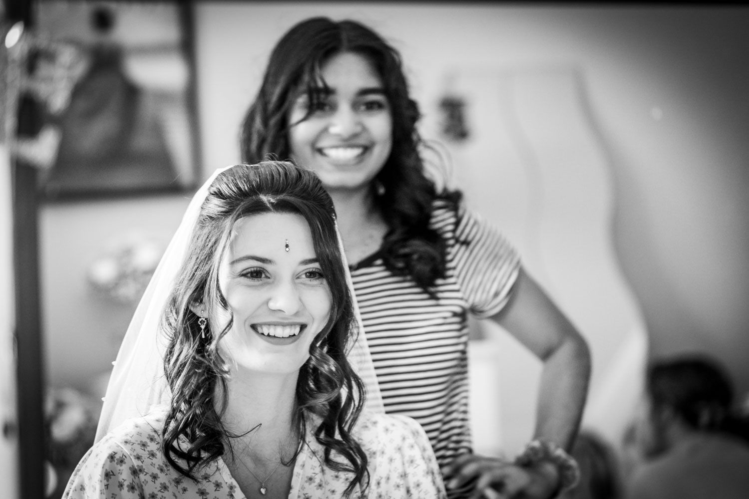 A black and white candid photograph capturing joyful expressions during wedding preparations.