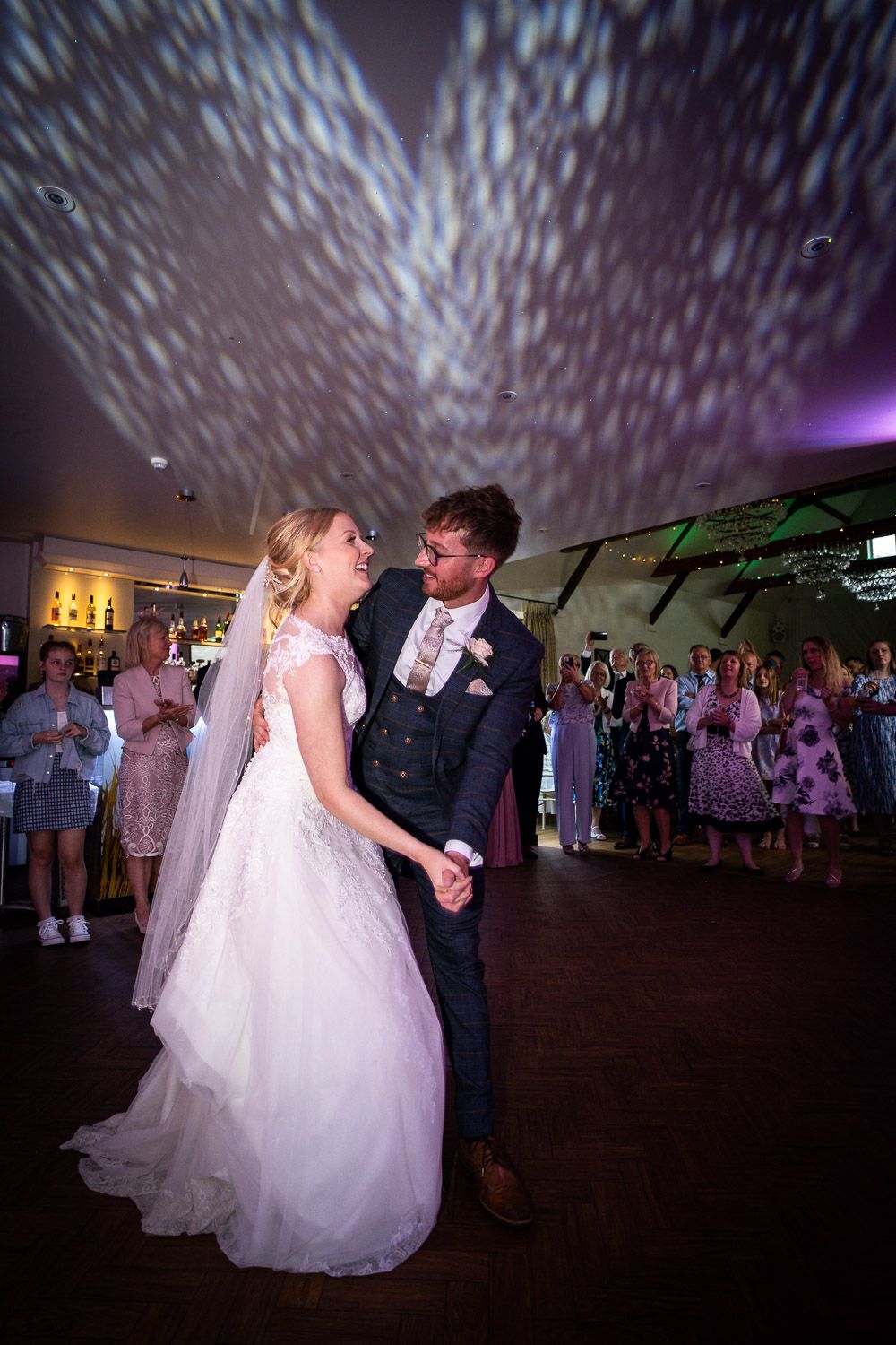 A couple shares their first dance at their wedding reception under dramatic lighting and a starlit effect on the ceiling.