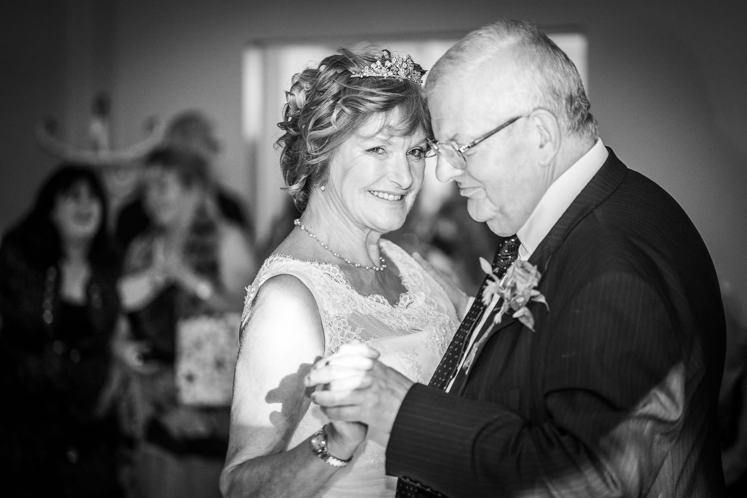 A tender moment captured in black and white as an older couple shares a dance at an elegant formal event.