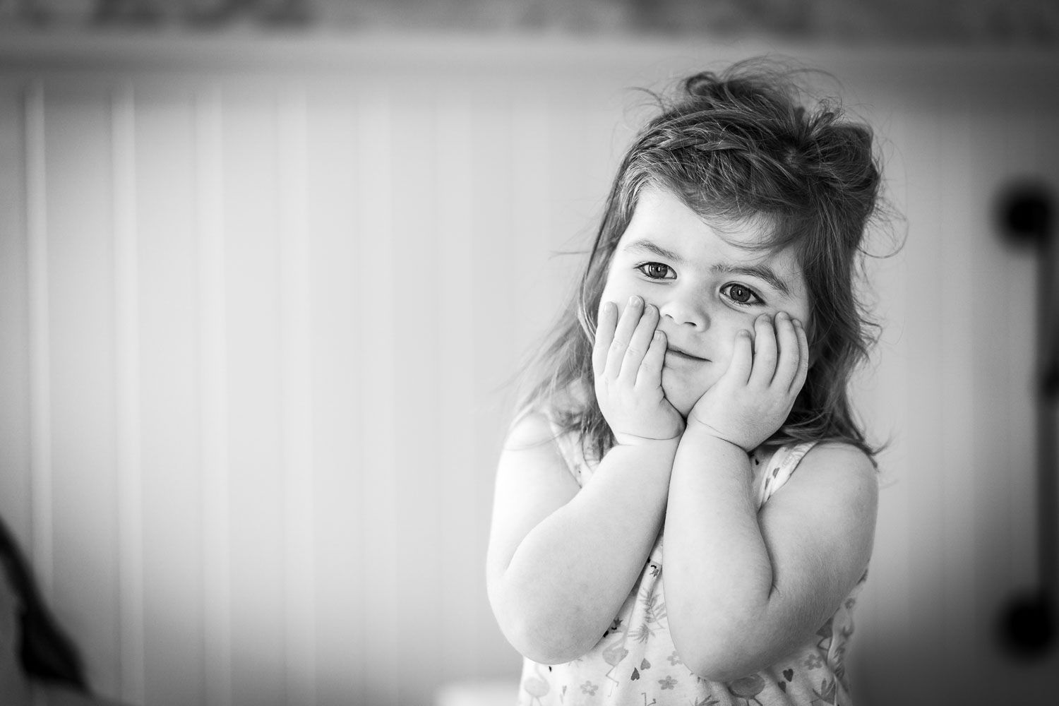 Black and white portrait of a small child with hands on cheeks expressing surprise and wonder.
