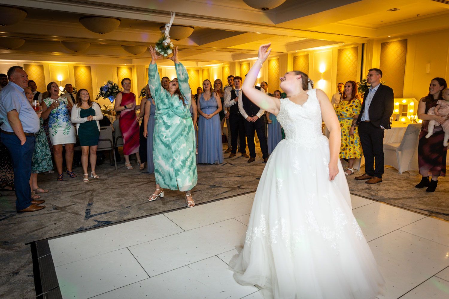 Wedding reception celebration with guests dancing and cheering in elegant ballroom setting.