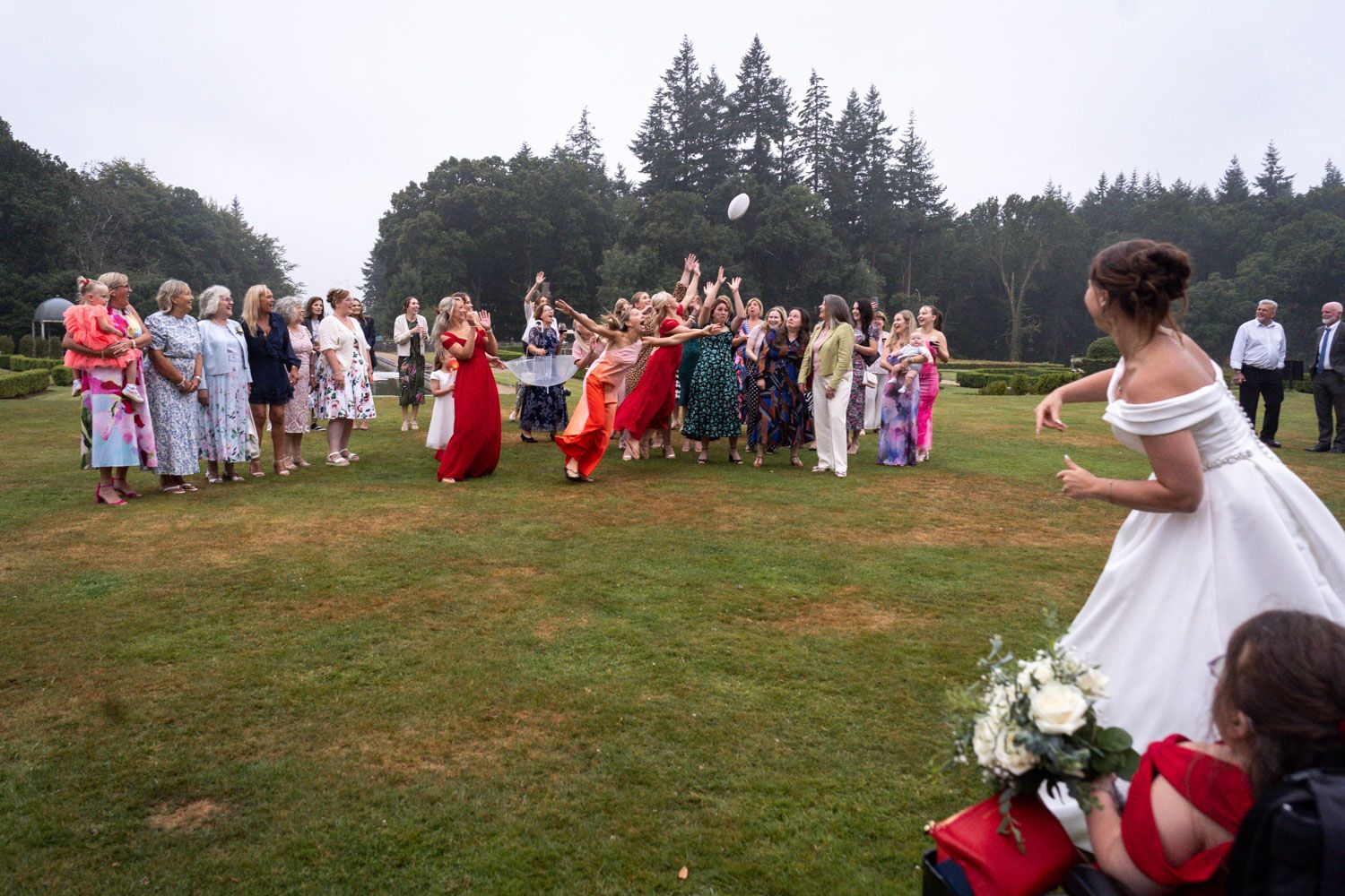 A wedding party gathers on a grassy outdoor field with guests wearing red and white attire.